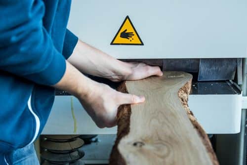 iemand schuift houten plank zonder beveiliging in gevaarlijke machine