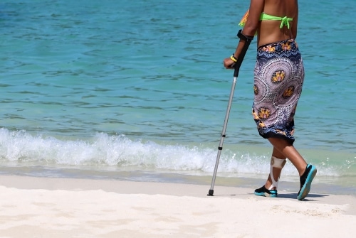 Vrouw loopt met kruk over het strand